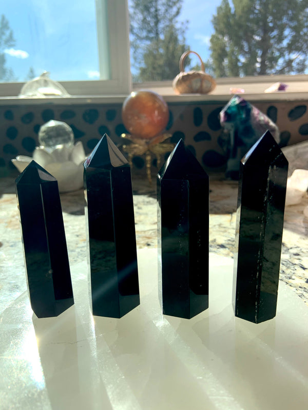 An array of black obsidian points shown in a group on top of a selenite plate with crystal spheres in the background. Choose your size from the dropdown menu.