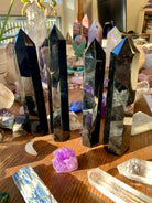 Angled view of four large Black Obsidian towers on a wooden table among a crystal collection — Root Chakra stones for protection & clarity.