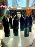 A collection of black obsidian points shown in a group on top of a selenite plate. Choose your size from the dropdown menu.