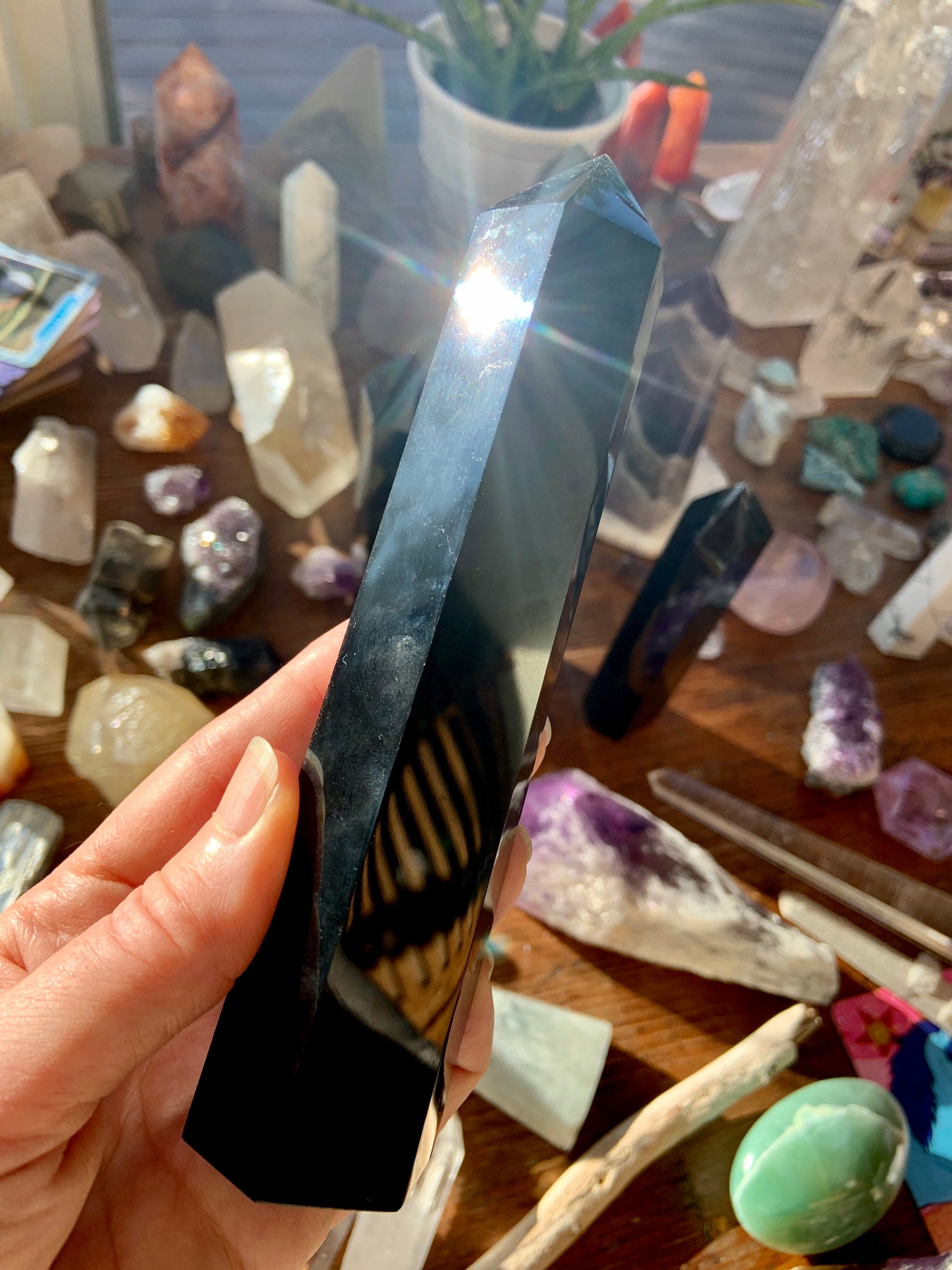 Hand holding large Black Obsidian tower with sunlight glint — polished crystal for spiritual protection & grounding energy.