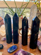 Row of four large Black Obsidian towers on a wooden table — grounding crystals for protection & energetic boundaries.