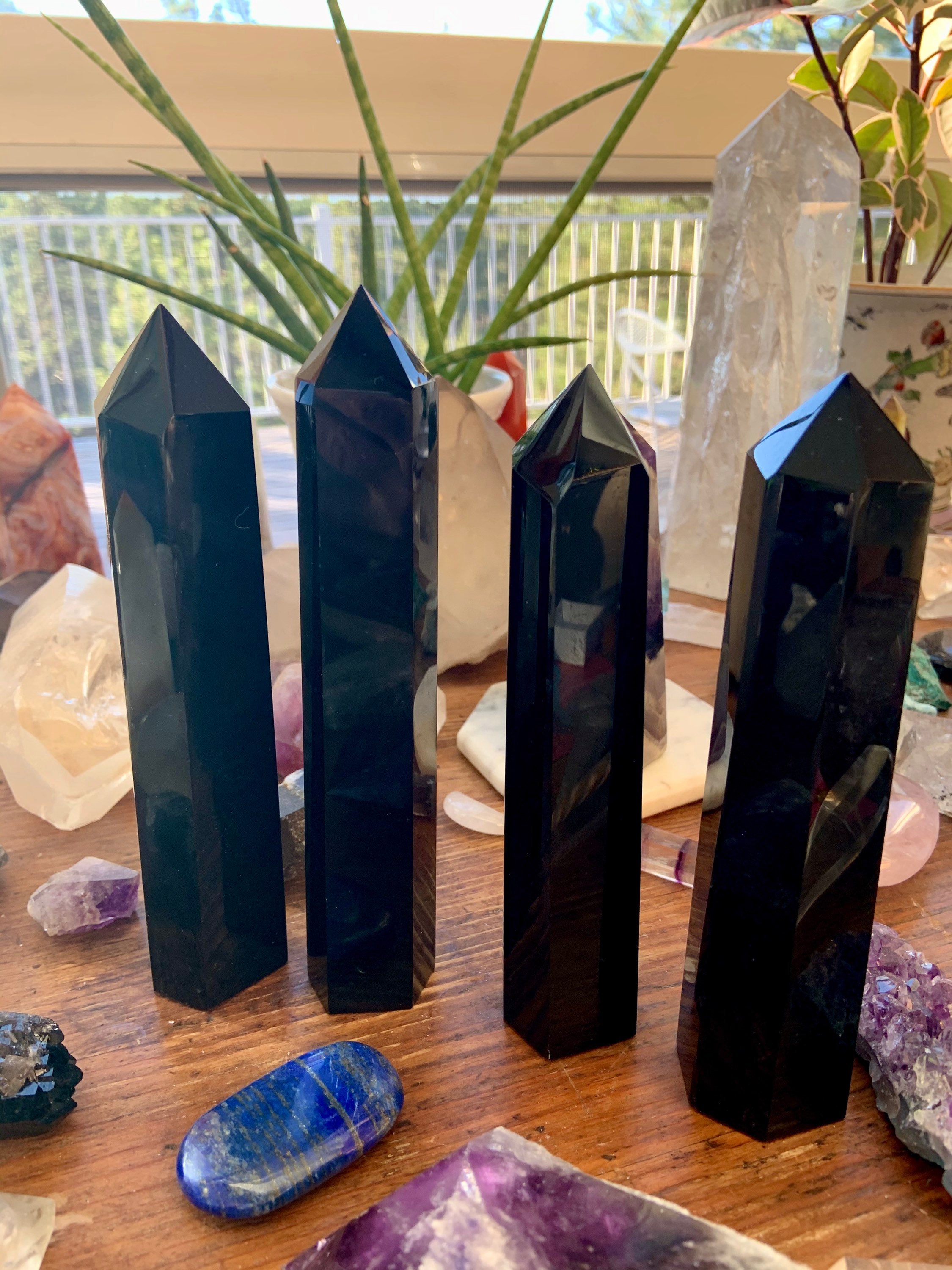 Row of four large Black Obsidian towers on a wooden table — grounding crystals for protection & energetic boundaries.