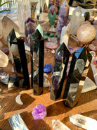 Another angled view of four large Black Obsidian towers on a wooden table with other crystals — grounding stones for energy protection.
