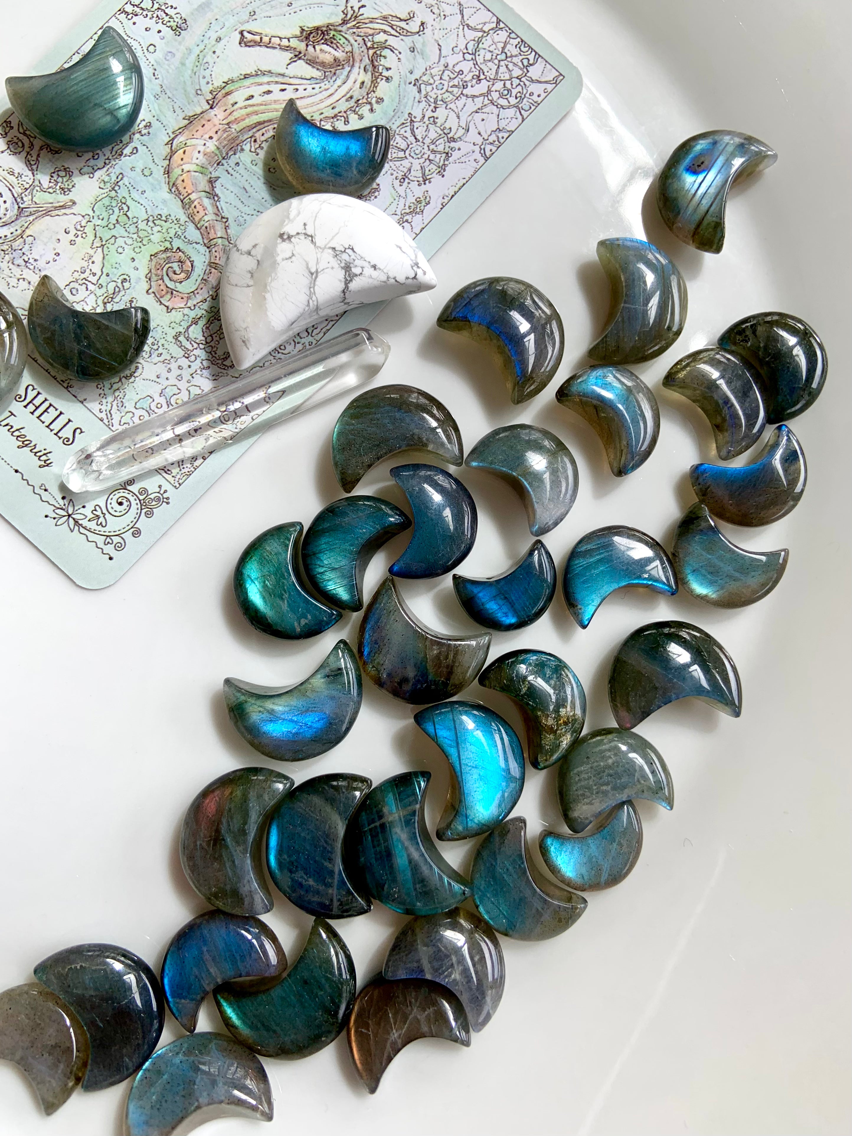 Overhead view of Labradorite crescent moons with tarot card, howlite moon & quartz point — flatlay crystal assortment for intuitive energy work.