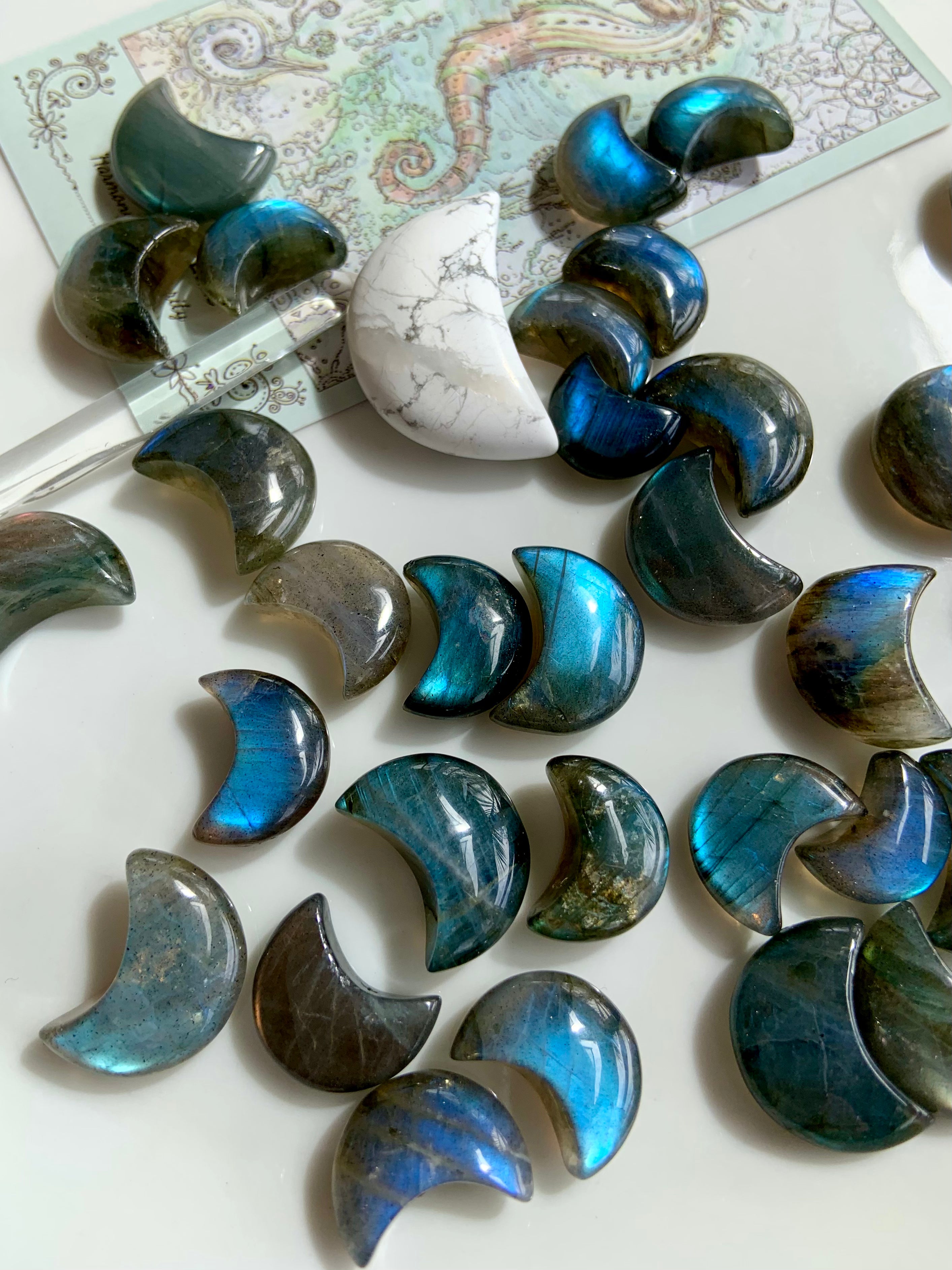 Flatlay of Labradorite mini moon crystals with a tarot card, howlite moon & quartz point — celestial crystal arrangement for insight & healing rituals.