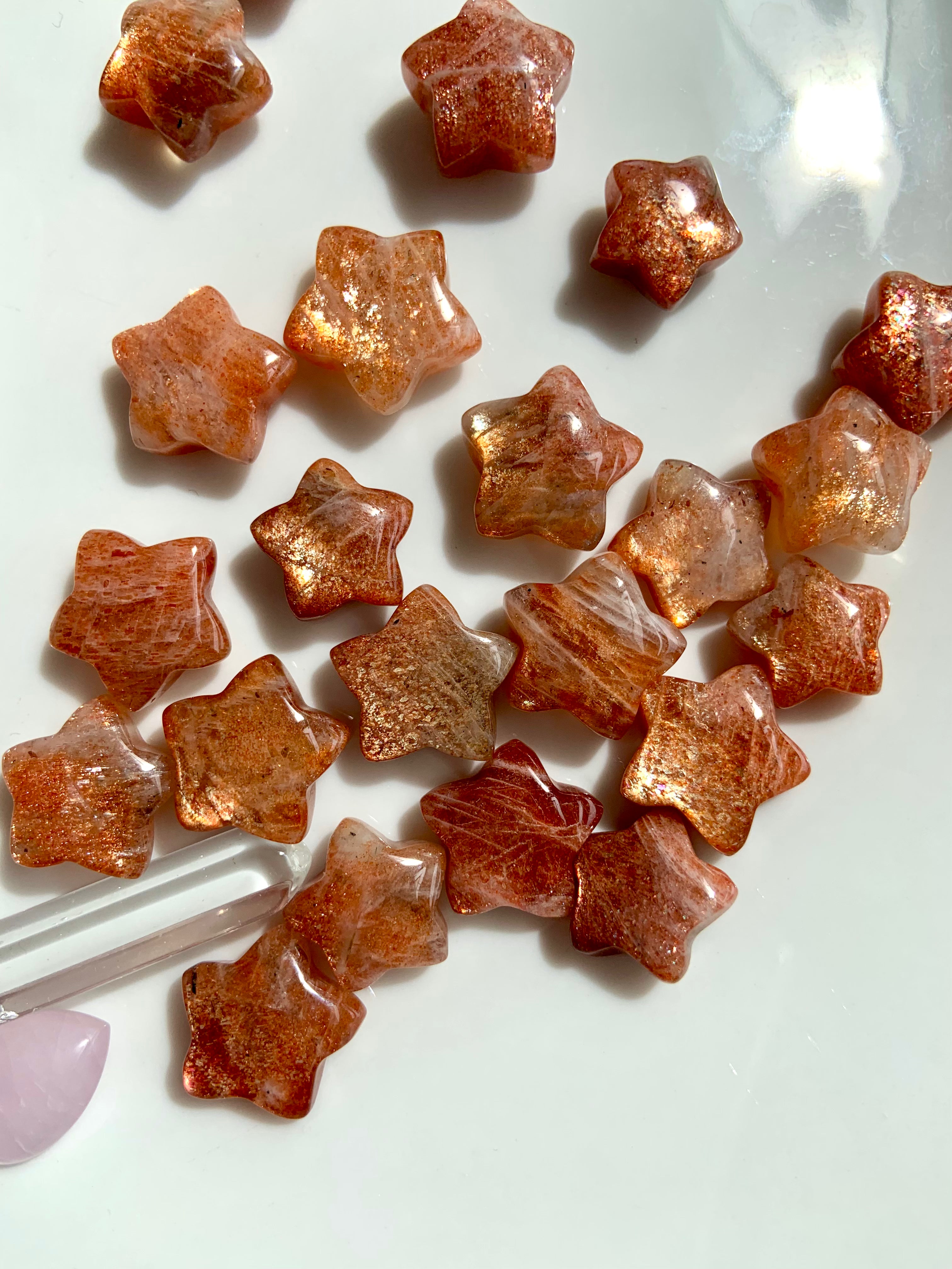 A collection of star-shaped Arusha Sunstone crystals with a golden orange hue and sparkling inclusions, displayed on a white surface.